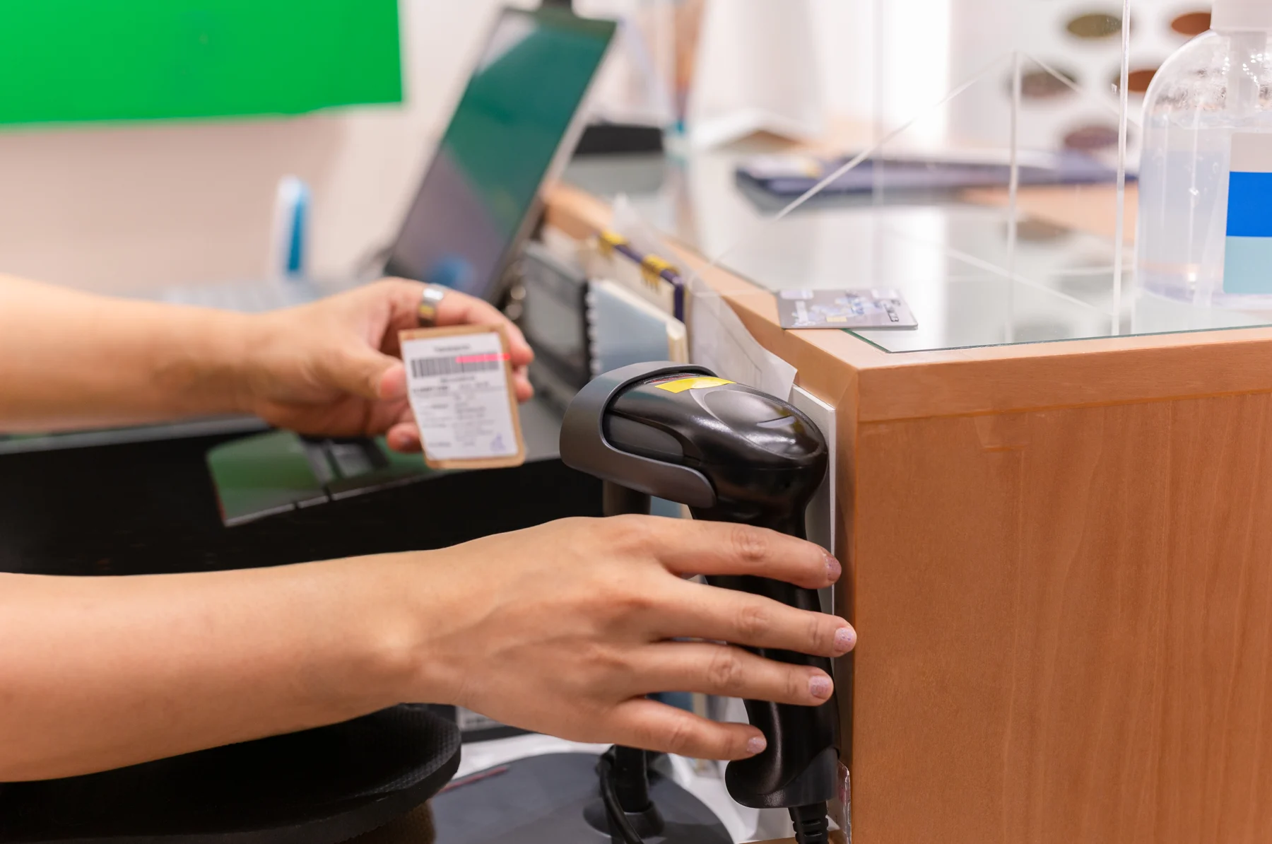 Hands holding a barcode scanner beside a product and checkout register.