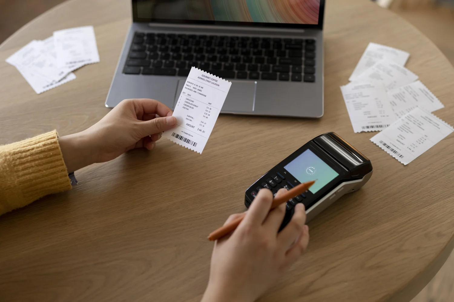 Hands checking a receipt beside a laptop and other sales records